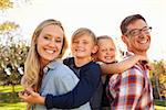 Parents carry their two young kids piggyback in a park, close up