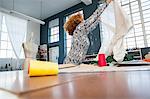 Mature female fashion designer holding up textile by workshop table