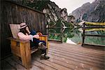 Woman relaxing on wooden chair, Lago di Braies, Dolomite Alps, Val di Braies, South Tyrol, Italy