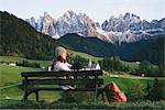 Woman relaxing on park bench, Santa Maddalena, Dolomite Alps, Val di Funes (Funes Valley), South Tyrol, Italy