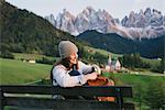 Woman relaxing on park bench, Santa Maddalena, Dolomite Alps, Val di Funes (Funes Valley), South Tyrol, Italy