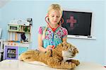 Girl pretending to be vet examining toy tiger using stethoscope