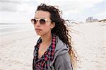 Young woman in sunglasses strolling alone on windy beach, Western Cape, South Africa