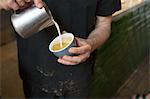 Male barista's hands pouring milk into coffee cup in cafe