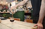 Male barista's hands pouring black coffee into brandy glass in cafe
