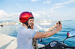 Young moped couple taking selfie at harbour, Split, Dalmatia, Croatia