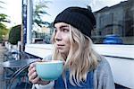 Young woman sitting outside cafe, drinking cup of tea