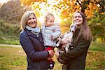 Portrait of senior woman with daughter, granddaughter and dog in autumn park