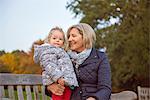 Senior woman sitting with toddler granddaughter in autumn park