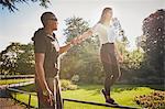 Woman holding hands with  personal trainer walking on park fence