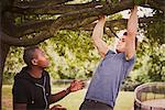 Personal trainer instructing man on pull ups using park tree branch