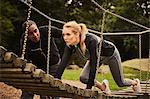 Personal trainer instructing young woman crawling on playground equipment in park