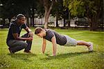 Personal trainer instructing young man doing push ups in park