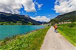 Rear view of senior man cycling by lake in Vinschgau Valley, South Tyrol, Italy