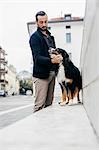 Mid adult man petting dog on wall in city