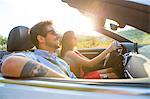 Young couple driving on sunlit rural road in convertible, Majorca, Spain