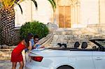 Young couple leaning against convertible looking at map, Calvia, Majorca, Spain