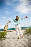 Mature woman with outstretched arms and standing on a beach.