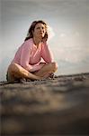 Mid-adult woman sitting with crossed legs on a beach.