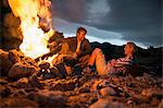 Young couple relaxing and laughing beside glowing campfire.