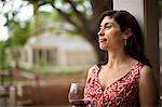 Contented middle-aged woman smiles peacefully as she relaxes with a glass of red wine and looks at the view from her back doorstep.
