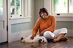 Middle-aged woman smiles and relaxes by petting her dog on the floor.