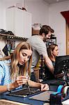 A man standing behind two women sitting working on circuitry in a technology lab.