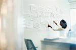 A woman standing in an office arranging pieces of paper pinned on a whiteboard.