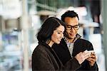 A young man and woman holding a cellphone together and looking at the screen.