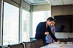 Two men standing at a table in a meeting room looking at an open book together.