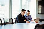 Two men at a table in a meeting room looking at a laptop computer.