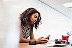 A young woman sitting in a classroom at a table and looking down at a cellphone.