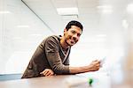 A young man sitting in a classroom leaning on a desk and smiling.