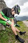 Young man with injured leg sitting on rock with bicycle, Bavaria, Germany