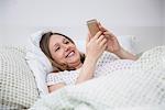 Pregnant woman lying in bed and using on mobile phone, Munich, Bavaria, Germany