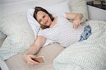 Pregnant woman lying in bed and taking selfie on mobile phone, Munich, Bavaria, Germany
