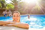 Woman in swimming pool resting on poolside looking at camera smiling