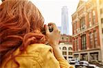 Young female tourist with long red hair photographing One World Trade Centre, Manhattan, New York, USA