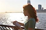 Young female tourist with long red hair looking at guidebook on waterfront, Manhattan, New York, USA