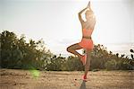 Young woman exercising outdoors, standing in yoga pose