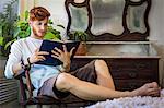 Young man with red hair, sitting in chair, reading book