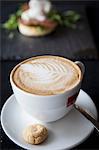 Cup of cappuccino with biscuit on table