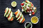 Smoked fish and avocado open sandwiches with salad and dipping sauces on slate, overhead view