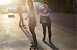 Young man pushing young female skateboarder on sunlit street