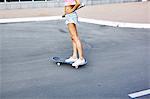 Young woman skateboarding along road, low section