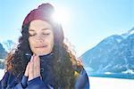 Portrait of woman in knit hat practicing yoga, meditating in snow covered sunlit landscape, Austria