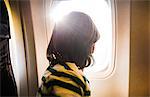 Boy on airplane looking through sunlit airplane window