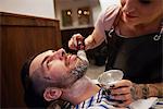 Woman applying shaving cream to man's beard