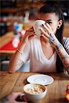 Tattooed woman in cafe drinking coffee looking at camera