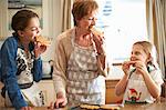 Senior woman and granddaughters eating freshly baked Christmas tree cookies